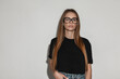 Glamour beautiful young woman model with vintage eyewear glasses in fashion black t-shirt mock-up stands near white wall. Trendy girl with stylish clothes