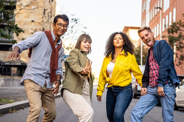 Multiracial group of friends having fun walking in a foolish way by street, party mood, happy university students acting funny moves and steps, smiling young people dancng in the city street