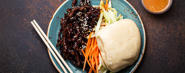 Wall Mural - Chinese traditional dish sweet and sour deep fried glazed pork with vegetables and steamed bao bun on plate with on rustic concrete background top view, Asian meal with chopsticks