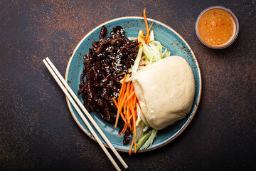 Wall Mural - Chinese traditional dish sweet and sour deep fried glazed pork with vegetables and steamed bao bun on plate with on rustic concrete background top view, Asian meal with chopsticks