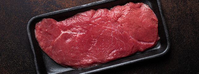 Canvas Print - Beef lean raw fillet steak in black plastic container on dark brown rustic concrete background from above flat lay, diet beef meat steak ready to be cooked