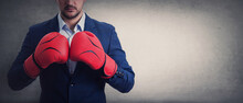 Close Up Businessman In Suit With Red Boxing Gloves Stands Ready In A Fighting Stance, Punching His Fists. Business Person Self Defence Concept, Isolated On Grey Wall With Copy Space.