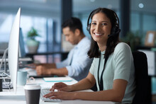 We Work To Make You Happy. Portrait Of A Young Woman Using A Headset And Computer In A Modern Office.