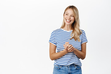 Wall Mural - People concept. Stylish modern girl, 25 years old, standing in assistant helpful pose, ready to offer help, listening to customer and smiling, standing over white background