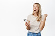 Enthusiastic young woman winning on mobile phone, rejoicing, using smartphone app, celebrating, triumphing on cellphone, white background