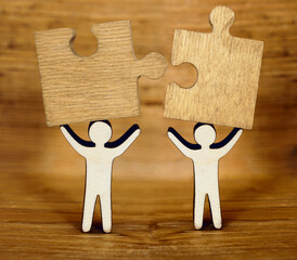 two wooden human figure holding in hands 2 puzzles. Real love, lover, couple concept. Two wooden figures, standing together isolated on wood board  background.