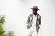 © mimagephotos - handsome african american man leaning against white wall with shirt and hat