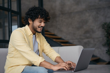 Young Indian freelancer copywriter working from home. Smiling handsome asian programmer using laptop computer typing on keyboard sitting at workplace. Student studying, online education concept