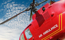 Red Helicopter Of Air Ambulance Isolated Against Blue Sky And Clouds  Background. Detail Of The Helicopter Blades. First Aid And Emergency Concept