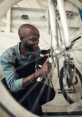 Wall Mural - Making this bike feel brand new. Shot of a handsome young man crouching alone in his shop and repairing a bicycle wheel.