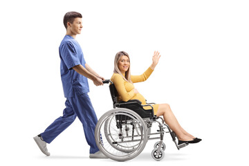 Wall Mural - Full length profile shot of a male nurse pushing a pregnant woman waving and sitting in a wheelchair