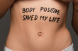 © LIGHTFIELD STUDIOS - cropped view of young woman with body positive saved my life lettering on belly isolated on grey