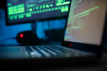 Background image of various computer equipment with programming code on screens on table in dark room, cyber security concept