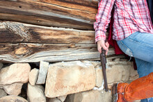 Cowgirl Holding A Revolver Pistol, Leaning Against A Weathered Wooden Ghost Town Wall, Wearing Red Plaid, Denim Dungarees, And Cowboy Boots, Angle Shot