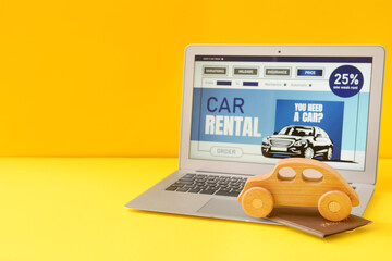 Wall Mural - Laptop with open page of car rental site, wooden toy and passport on yellow background