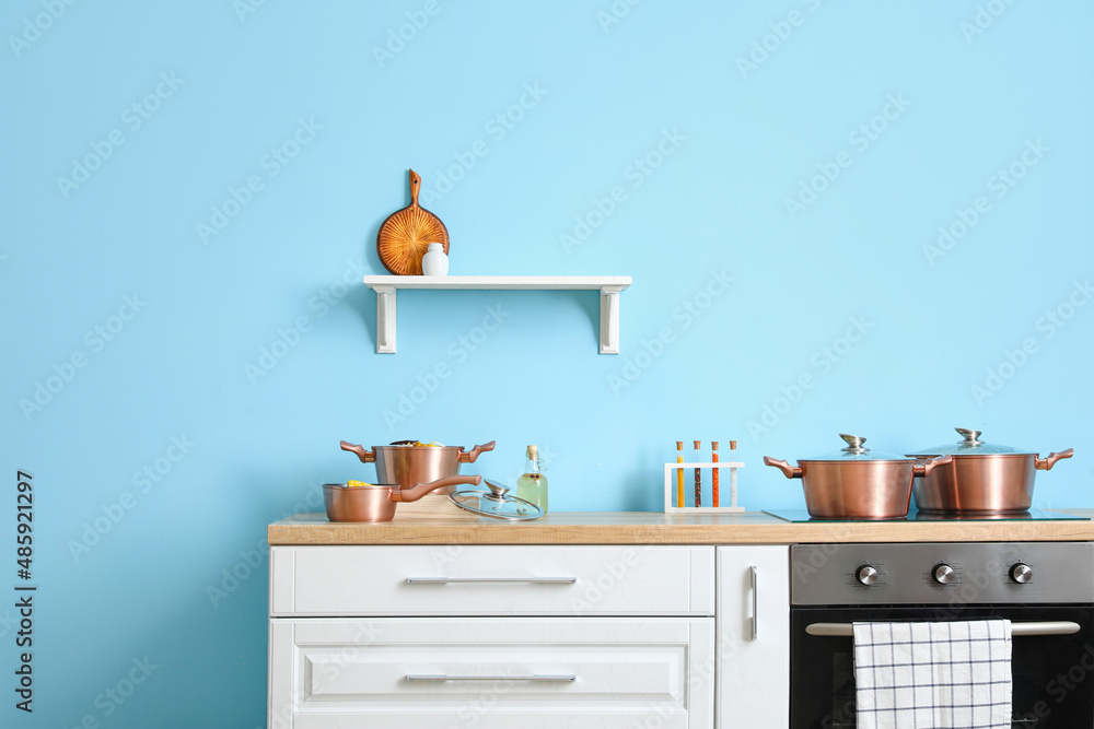 Modern kitchen with cooking pots and shelf near color wall