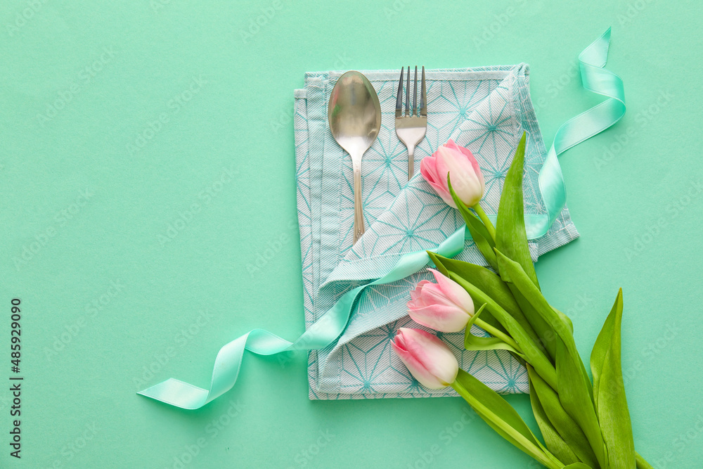 Stylish cutlery with tulip flowers on turquoise background