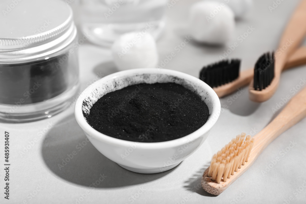 Bowl with activated charcoal tooth powder and toothbrushes on light background, closeup