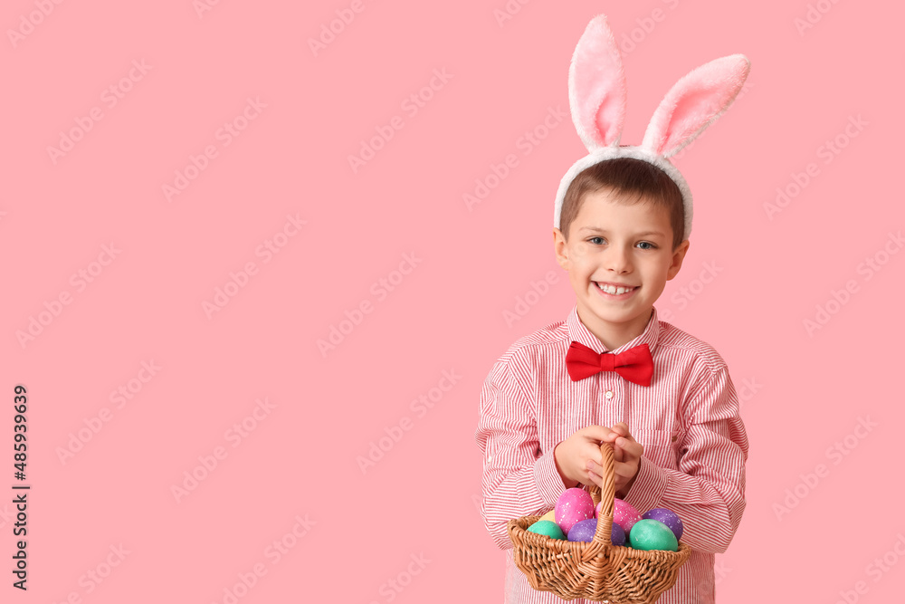Funny little boy with bunny ears and Easter basket on pink background