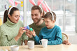 © Pixel-Shot - Happy parents with their little son in bunny ears breaking Easter eggs at table