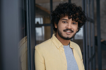 Young smiling Indian man looking at camera standing in modern office. Portrait of handsome successful asian student. Education concept   