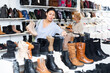 Asian woman, who came to a shoe store for shopping, chooses winter boots in the style apreski