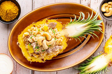 Wall Mural - Pineapple Fried Rice with pork, egg, garlic, onion, spring onion, pepper and curry powder, cashew nut on top in oval ceramic plate on old white wood background, top view, Khao Pad Sapparod, Thai food