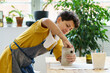 © DimaBerlin - Young female artisan concentrated on modeling jug from raw clay while pottery lesson or workshop in creative studio. Woman ceramic business owner making craft for sale in handmade potter retail store