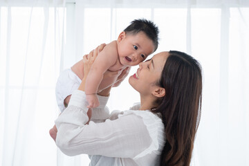 Happy family. Laughing mother lifting her adorable newborn baby son in air, copy space. asian mother lifting and playing with newborn baby, Health care family love together. Asian girl lifestyle.