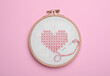 Canvas with embroidered heart and needle in hoop on pink background, top view