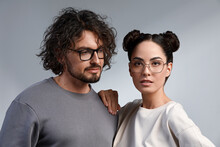 Fashion Models Couple Wearing Glasses. Sexy Woman And Handsome Young Man Portrait Over Lite Background. Attractive Fashion Boy And Girl Posing. Hairstyle, Haircut