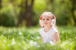 Cute little girl is listening to music in the spring park. Family summer outdoor lifestyle. Happy small kid in headphones sitting on green grass. Beauty nature at summer. Childhood happiness