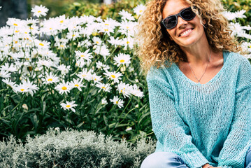 Wall Mural - Portrait of joyful beautiful adult woman with curly hair and sunglasses and garden park daisies flowers background Concept of people and leisure activity in spring season. Copy space on left