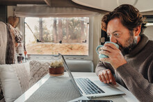 Mature Man Working On Laptop Computer Inside A Camper Van With Nature Outdoors View Outside The Window. Concept Of Freedom And Vanlife Lifestyle. Smart Remote Working  Online