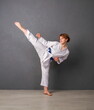 © sharpner - A young girl karateka in white kimono and a blue belt trains and performs a set of exercises against a gray wall
