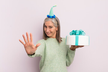 Wall Mural - middle age woman smiling and looking friendly, showing number five. bitrthday cake concept