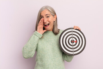 Wall Mural - middle age woman feeling happy,giving a big shout out with hands next to mouth. darts target concept