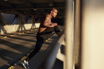 Wall Mural - Young black sportsman stretching on empty bridge