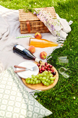 Wall Mural - leisure and drinks concept - close up of food, drinks and basket on picnic blanket on grass