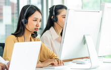 Asian Beautiful Attractive Female Call Center Stressful Working With Pressure With Headsets, Sitting, Monitoring At Computer Screen In Agency, Giving Service And Receiving Complaints Of Customers.