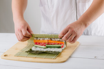 Wall Mural - the chef cook prepares sushi and wraps a letter to the nori in the roll, on white background