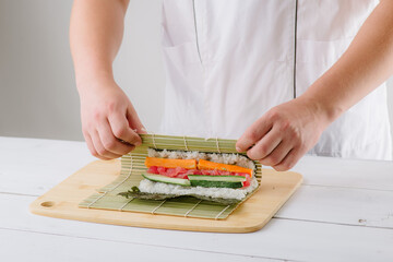 Wall Mural - the chef cook prepares sushi and wraps a letter to the nori in the roll, on white background