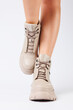 © DSMT - Female legs in beige leather shoes from the new collection on a white background female legs in fashionable shoes made of eco-leather spring 2022.