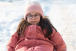 © PeterPike - A small child in winter clothes and a knitted hat and glasses looks ahead while sitting on a sled. Winter photo session outdoors