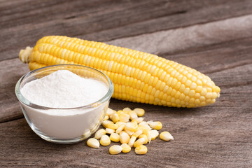 Corn starch in wooden bowl and fresh sweetcorn with kernels on wood table background. 