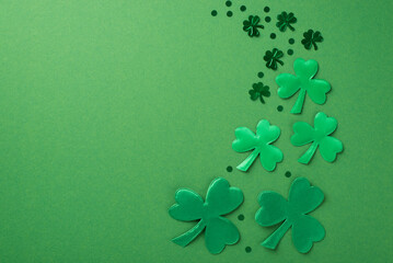 Top view photo of the green confetti different size and shades in shape of clovers and dots on the green isolated background blank space