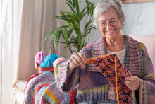 Senior Smiling Woman Sitting On Sofa At Home While Knitting And Looking At Her Work In Progress. Hobby, Retirement, Relax Concept For Elderly Female Wearing Glasses