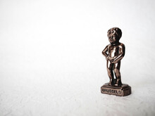 Manneken Pis Statue On White Background. Brussels Symbol. Miniature Bronze Figurine Of A Naked Boy Urinating Into A Pool. Metal Souvenir. Baby Pissing