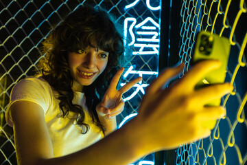 Wall Mural - A young woman with curly hair takes a selfie near a yellow metal grid and in neon lighting.