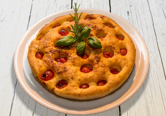 Wall Mural - Apulian focaccia, typical italian Bari pizza made with a dough of durum wheat flour and potatoes  with cherry tomatoes on top. In white plate on white wooden table